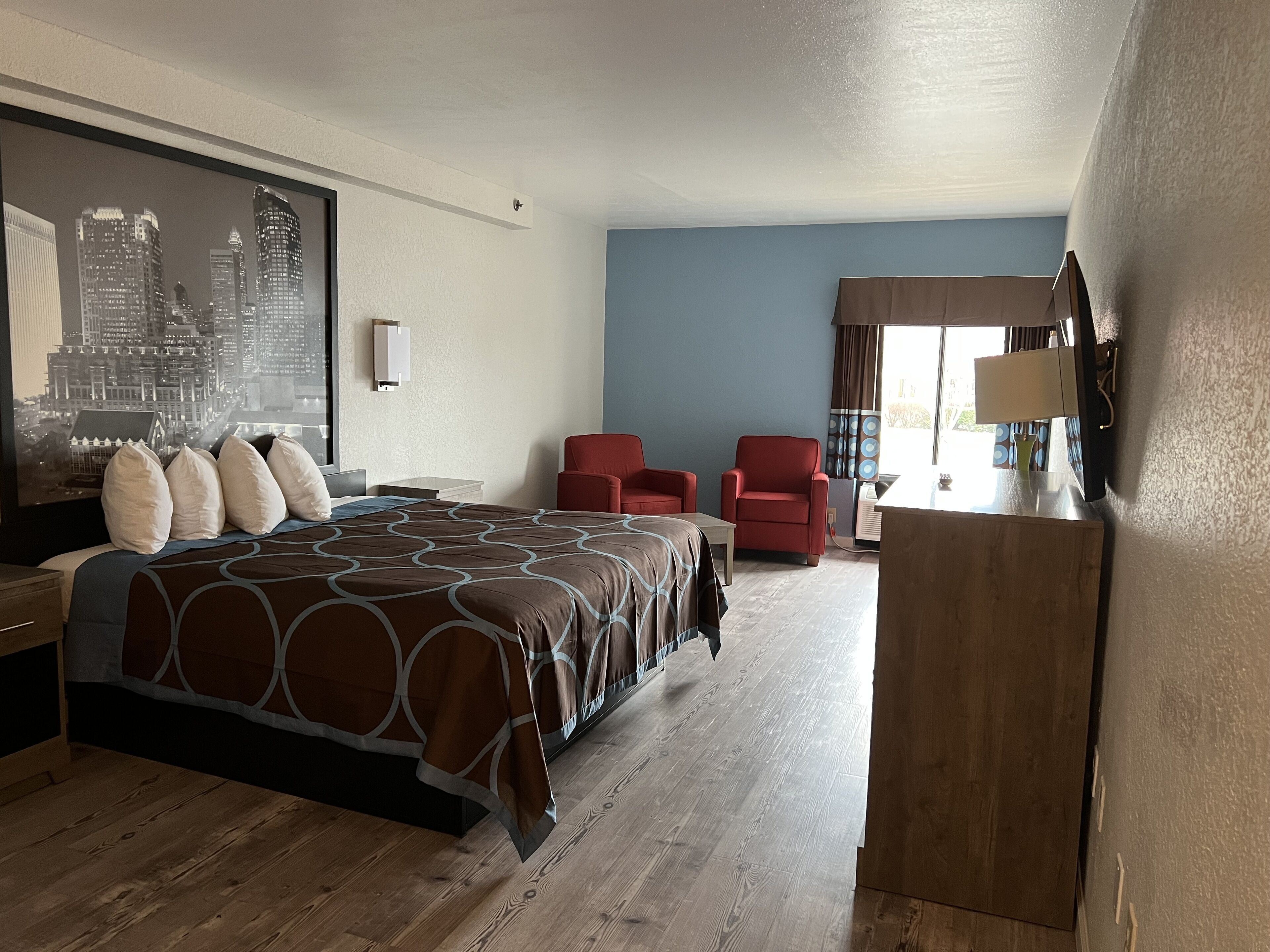 Habitación de hotel con una cama grande, dos sillas rojas, un escritorio y vista a la ciudad.