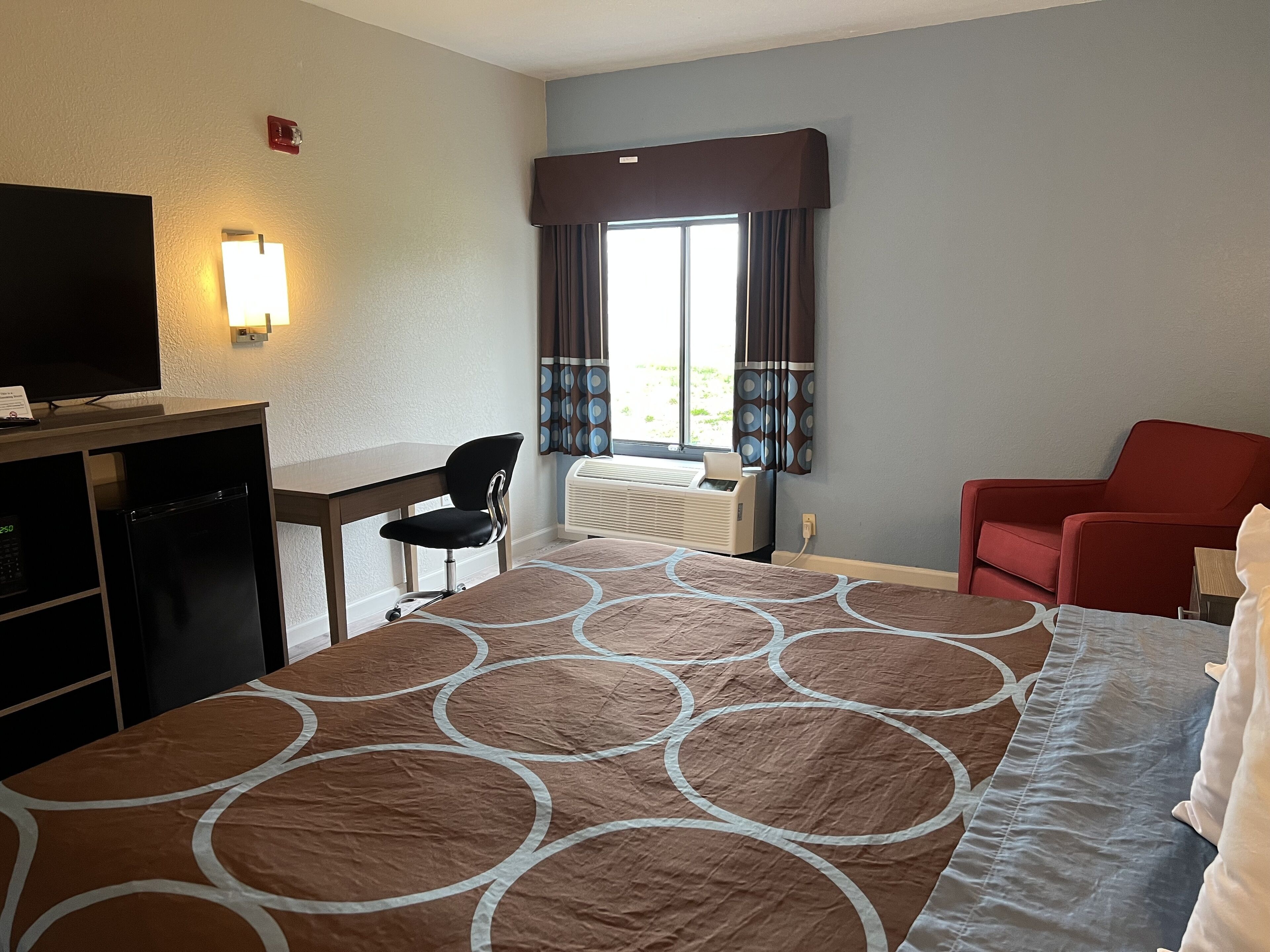 Una habitación de hotel con una cama, un escritorio, un televisor, una silla y un sillón rojo.