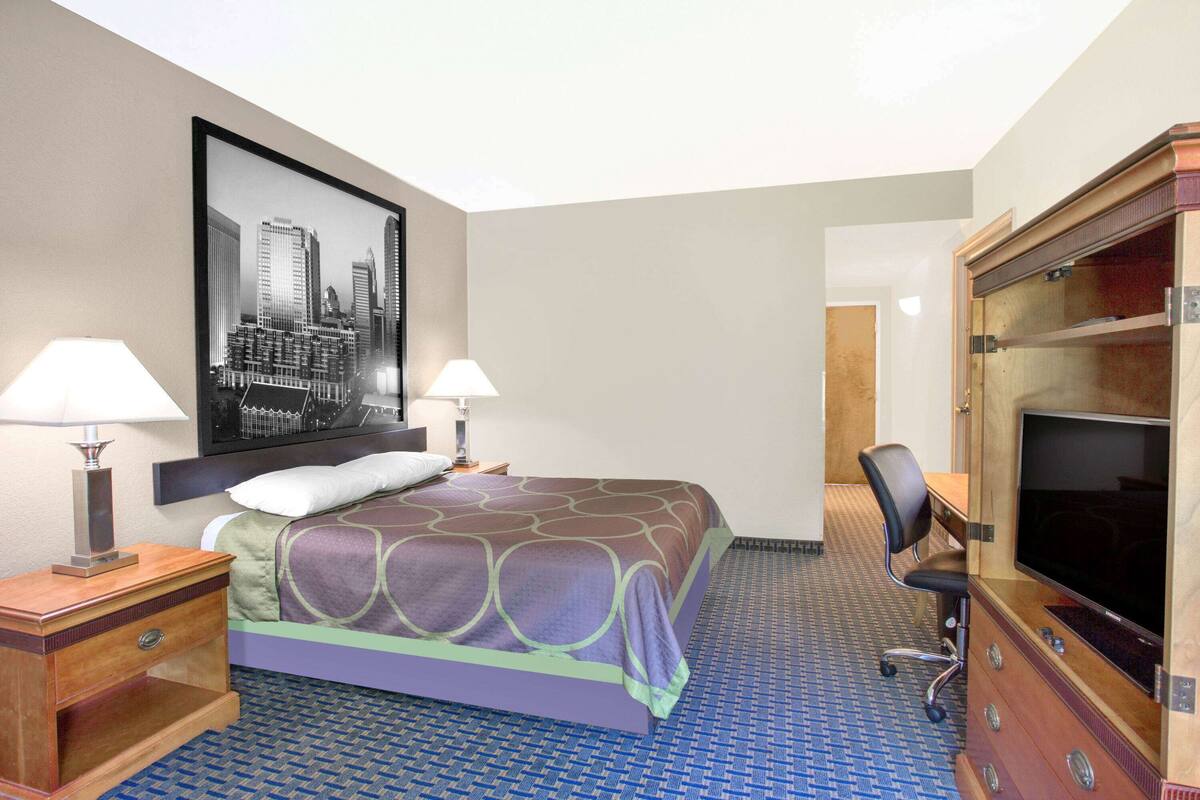 A hotel room with a bed, two bedside lamps, a television, and a desk with a chair.