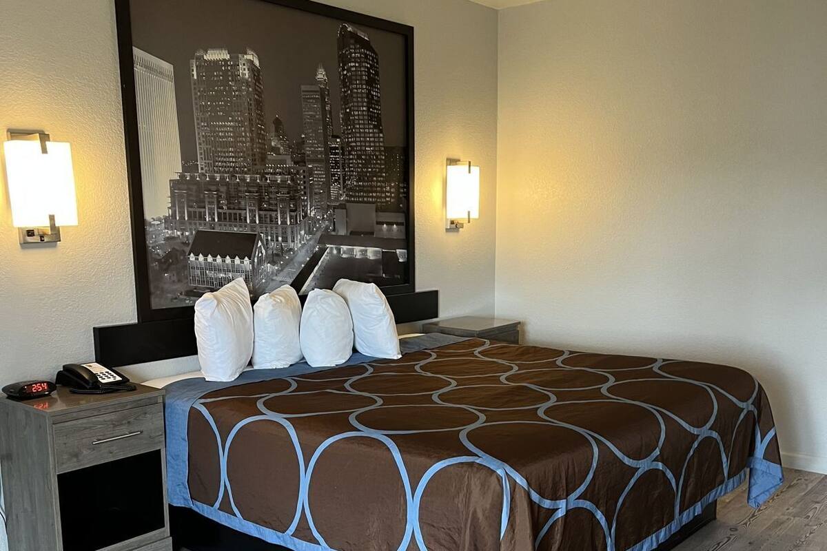 A hotel room with a bed, a nightstand, a cityscape painting, and two wall-mounted lights.