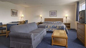 Une chambre d’hôtel avec un lit, un canapé, une table en bois, une télévision et deux lampes.