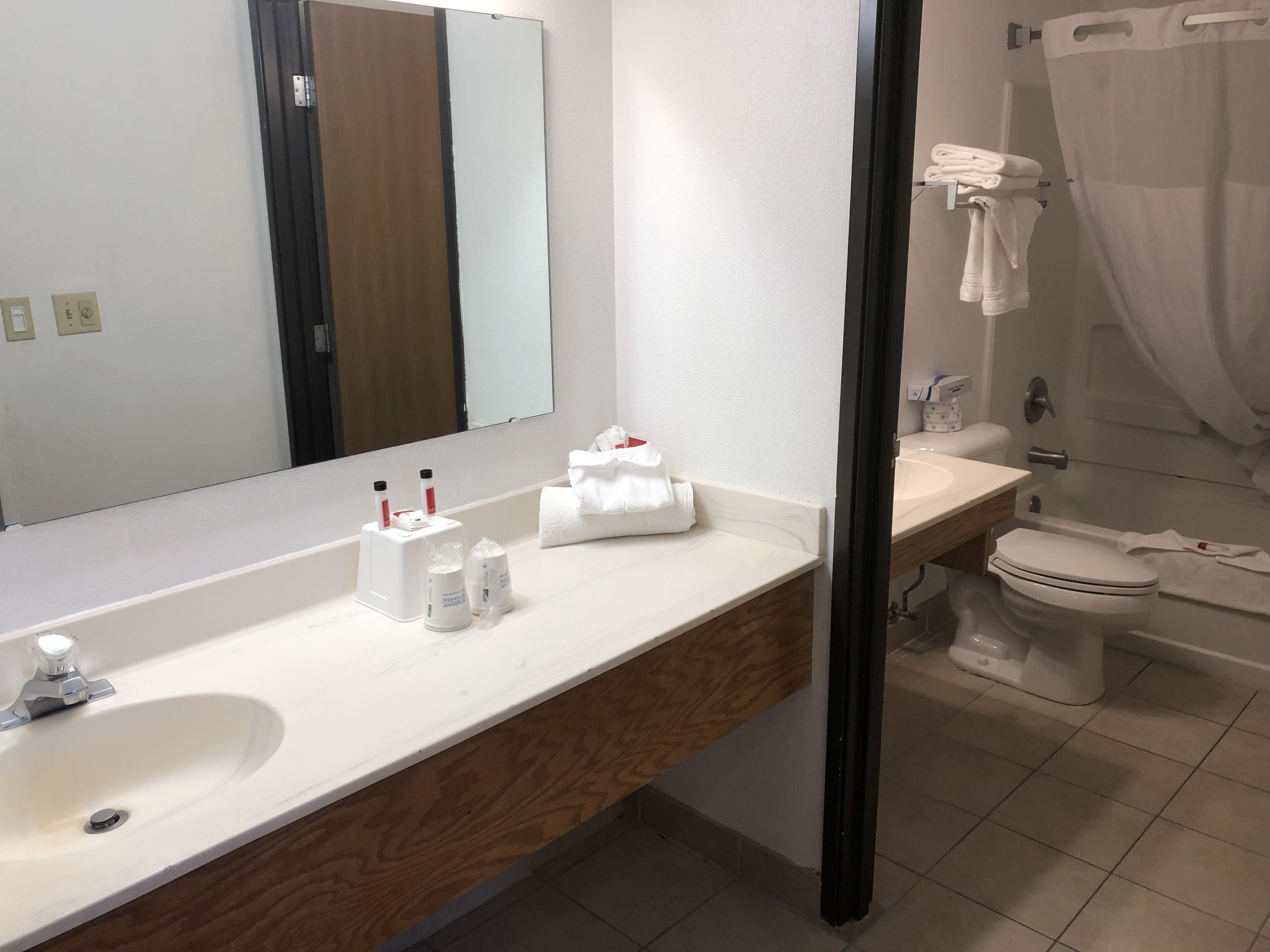 Kylpyhuoneessa on valkoinen pesuallas, peili ja wc-istuin. Tasoilla on hygieniatuotteita ja seinällä pyyheteline, jossa on pyyhkeitä.