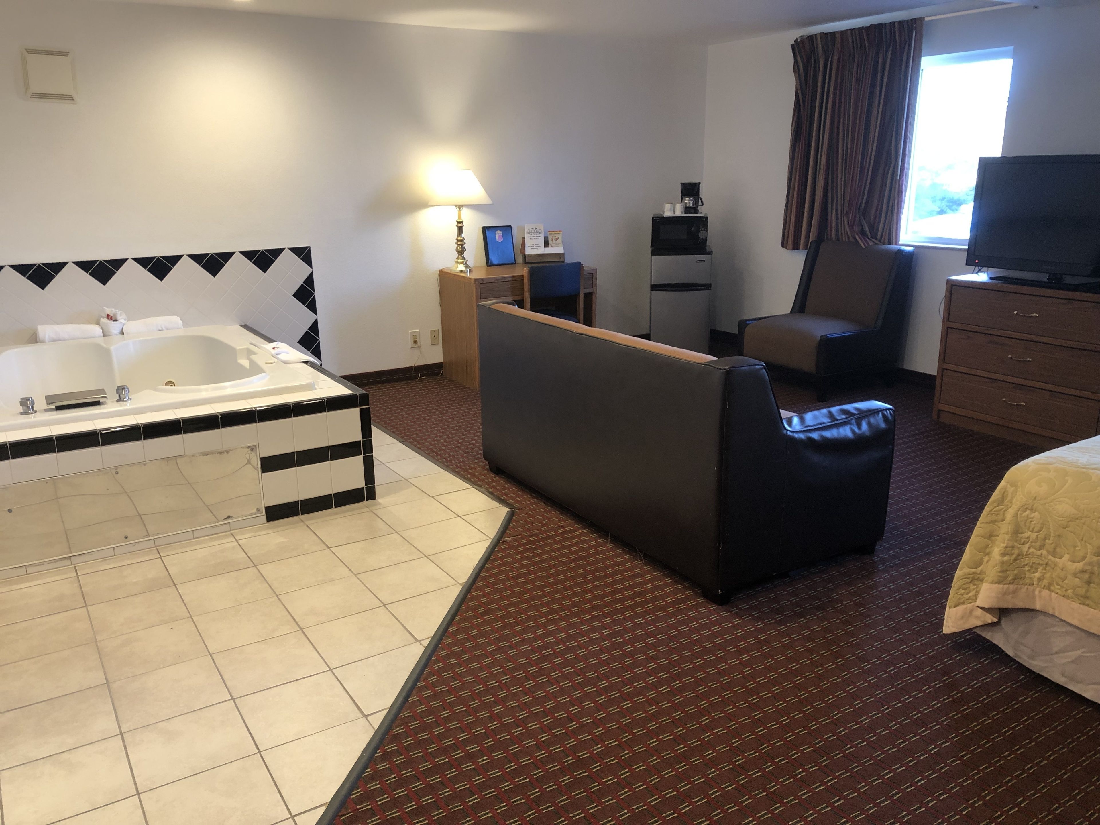 A hotel room with a large bathtub, a sofa, a television, and a desk with a computer.