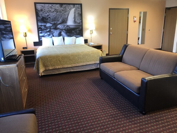 A hotel room with a bed, a sofa, a TV, and a large wall painting.