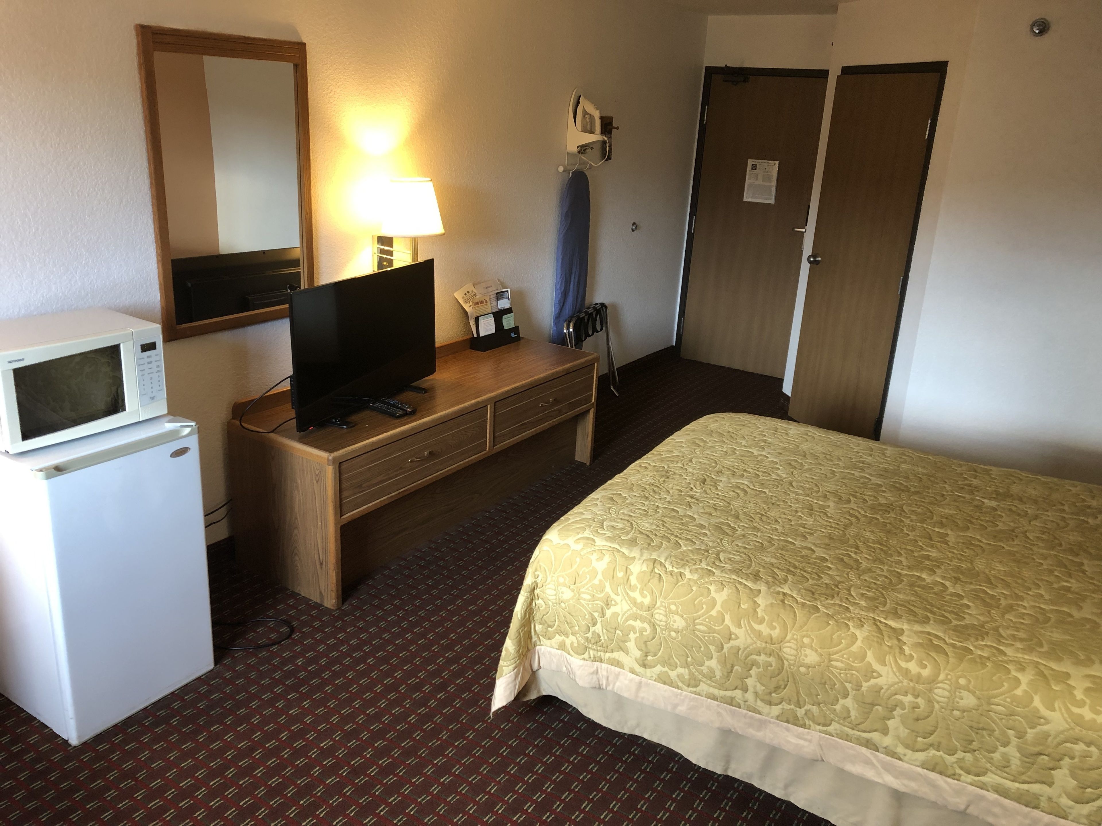 A hotel room with a bed, a television, a microwave, a dresser, and a door.