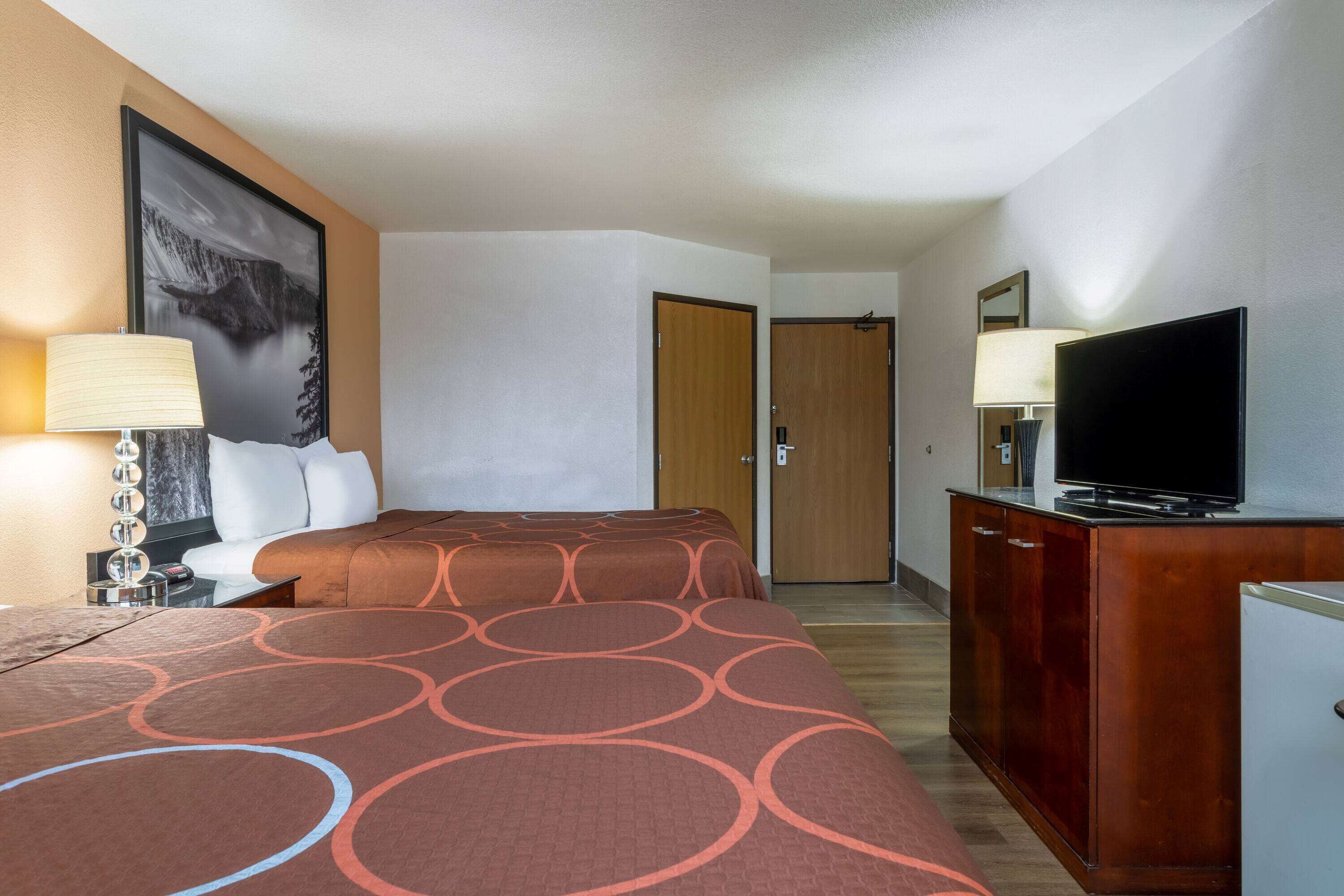 A hotel room with two beds, a TV on a wooden cabinet, and a painting on the wall.