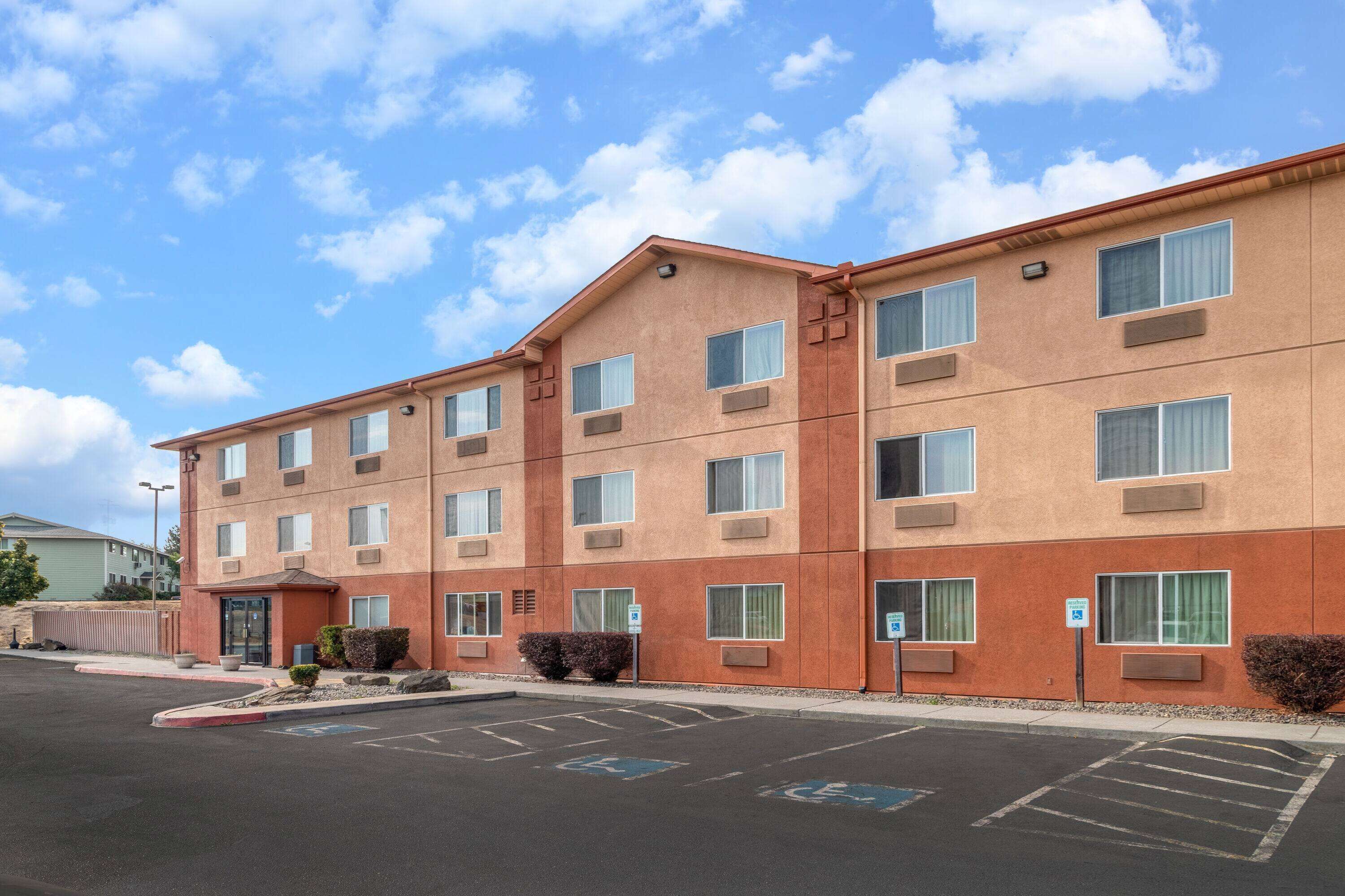 A multi-story hotel with a flat roof, large windows, and a parking lot with handicapped parking spaces.