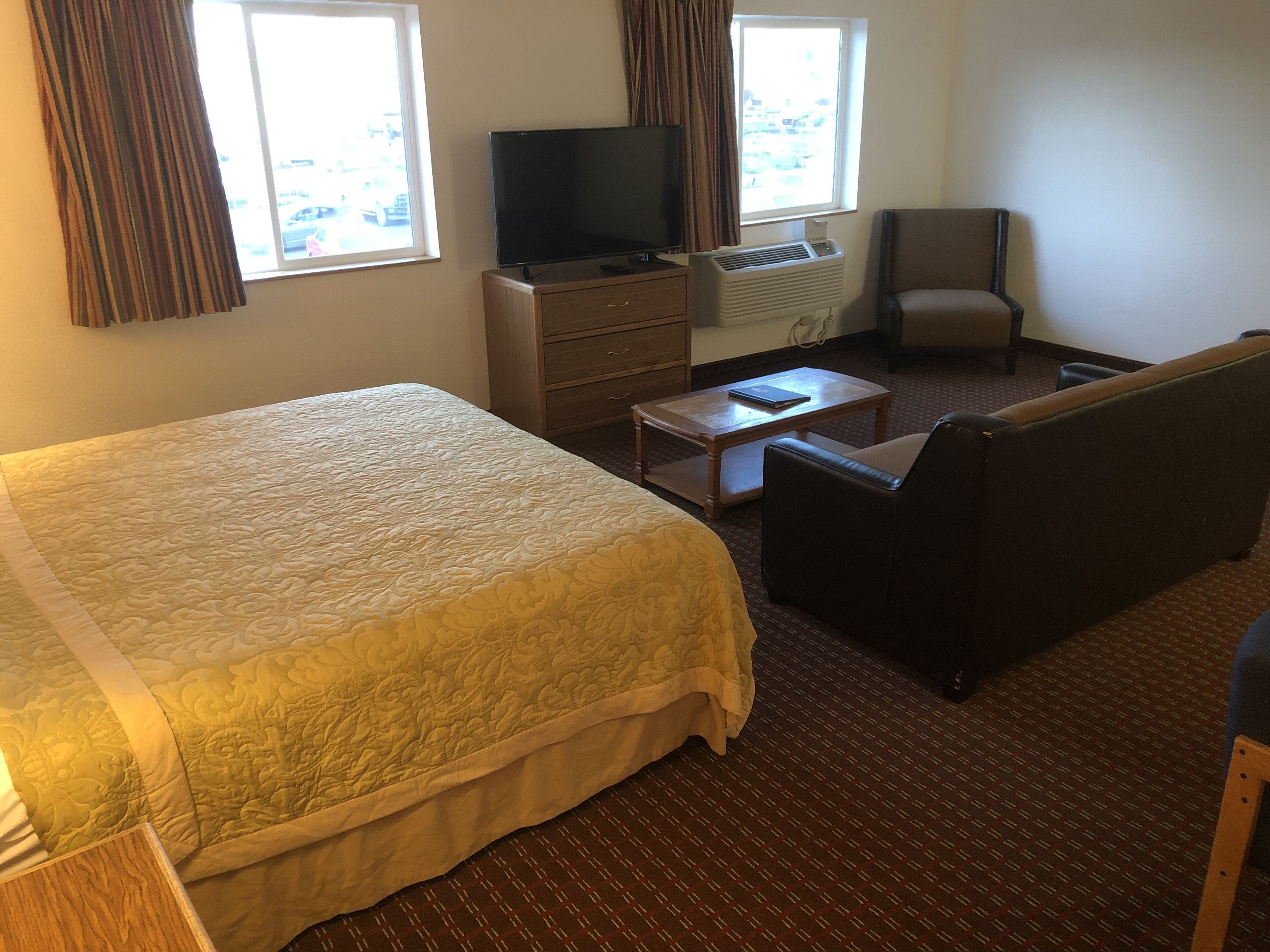Une chambre d’hôtel avec un grand lit, une télévision, un climatiseur, une petite table, une chaise et une fenêtre avec des rideaux.