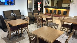 Un restaurant avec des tables et des chaises en bois, un canapé et un écran de télévision qui diffuse des images de personnes.