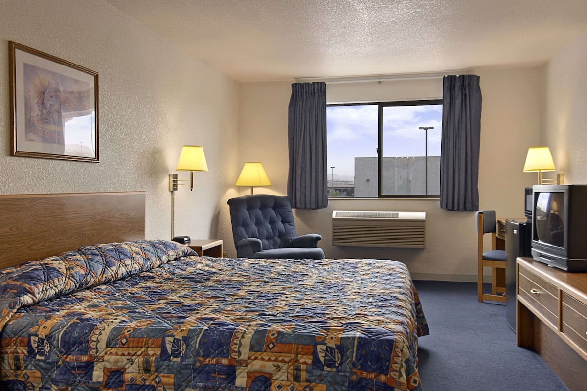 Ein Hotelzimmer mit einem großen Bett, einem Sessel, einem Schreibtisch mit Fernseher und einem Fenster mit Vorhängen.