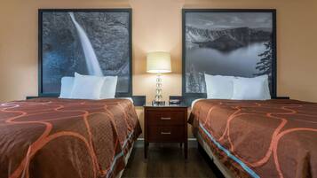 A hotel room with two beds, a nightstand with a lamp, and large framed pictures of a waterfall and a mountain landscape.