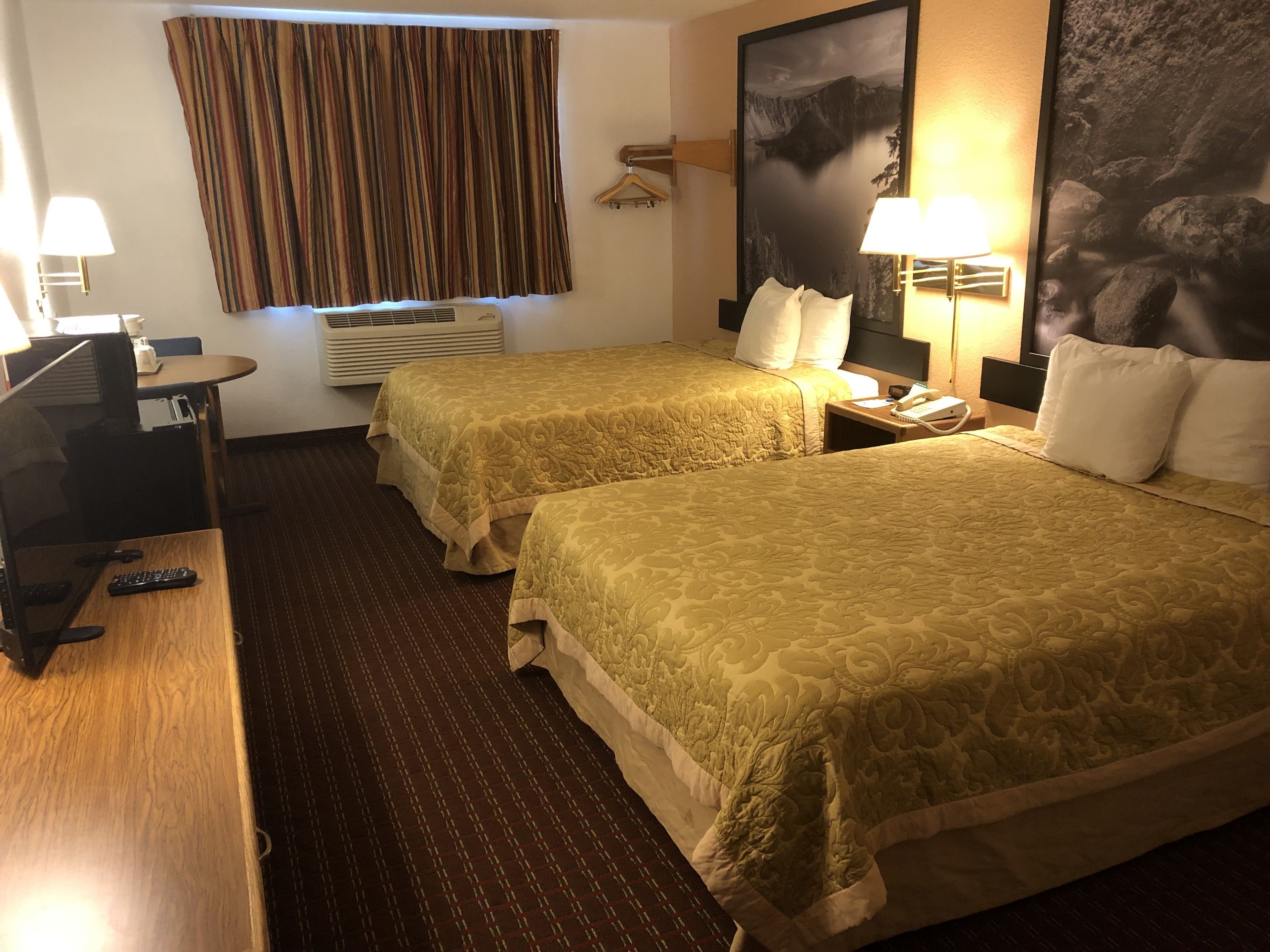 A hotel room with two beds, a desk with a computer, a telephone, and a window with curtains.