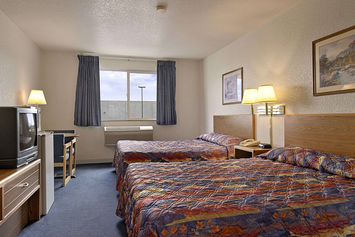 Ein Hotelzimmer mit zwei Betten, einem Fernseher, einem Schreibtisch und einem Fenster mit Vorhängen.