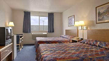 A hotel room with two beds, a TV, a desk, and a window with curtains.