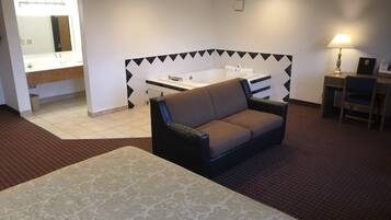 Une chambre d’hôtel comprenant un lit, un canapé, un bureau, une chaise, une lampe, ainsi qu’une salle de bain avec un lavabo et une baignoire.