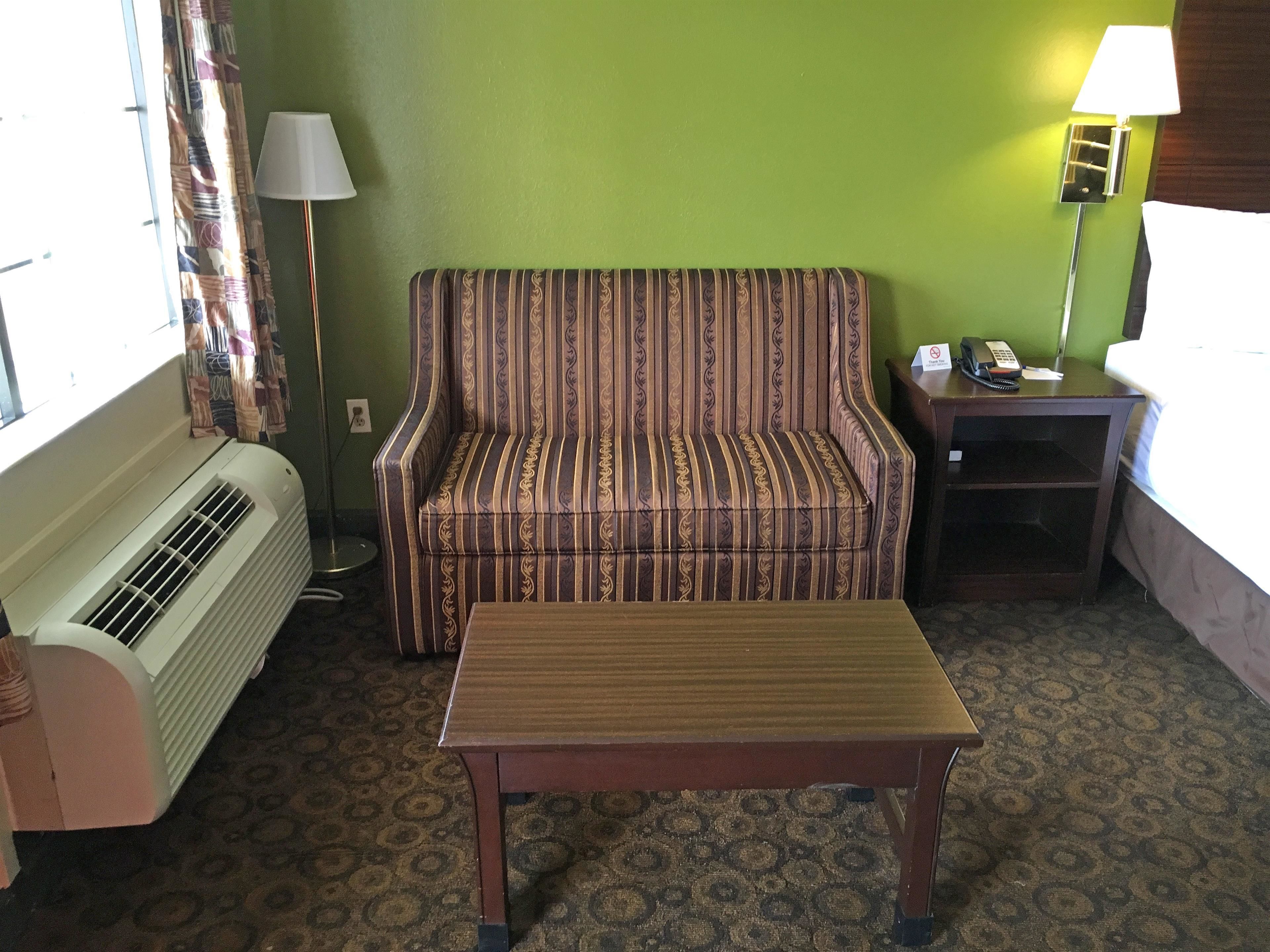 A hotel room with a striped sofa, a wooden table, a lamp, a telephone, and a heater.
