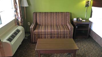 A hotel room with a striped sofa, a wooden table, a lamp, a telephone, and a heater.