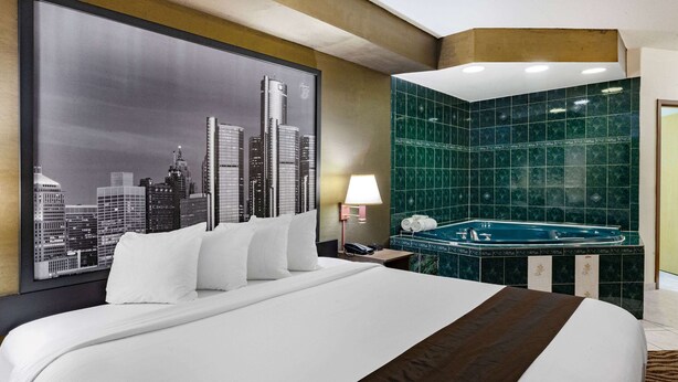 Habitación de hotel con una cama grande, un cuadro de un paisaje urbano, un jacuzzi con azulejos verdes y una mesita de noche con lámpara.