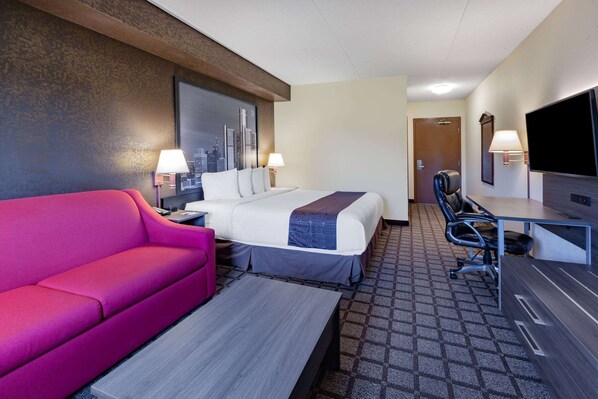 Una habitación de hotel con una cama, un escritorio, una silla, un sofá rosa y un televisor.