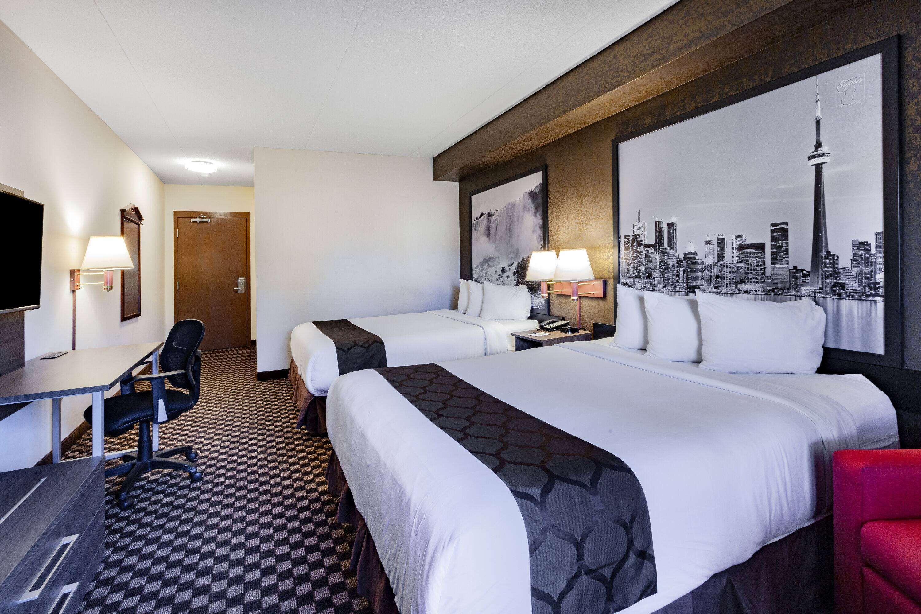 A hotel room with two beds, a desk, a chair, a TV, and a cityscape painting on the wall.