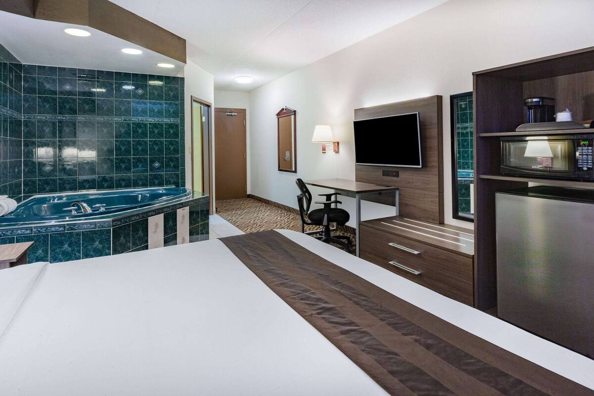 Une chambre d’hôtel dotée d’une baignoire en marbre, d’un téléviseur à écran plat, d’un four à micro-ondes et d’un petit coin repas.