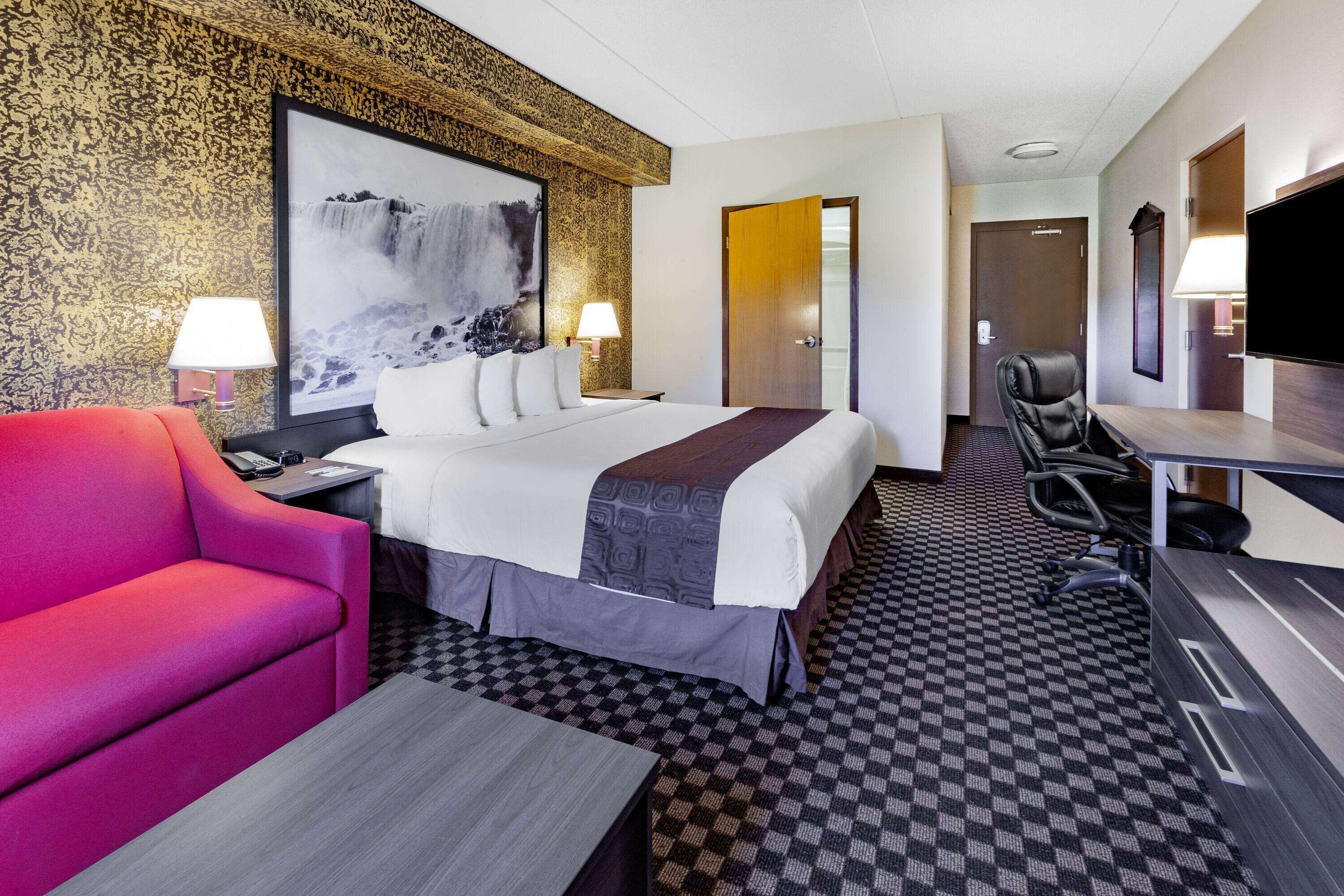A hotel room with a large bed, a red sofa, a desk, and a TV.