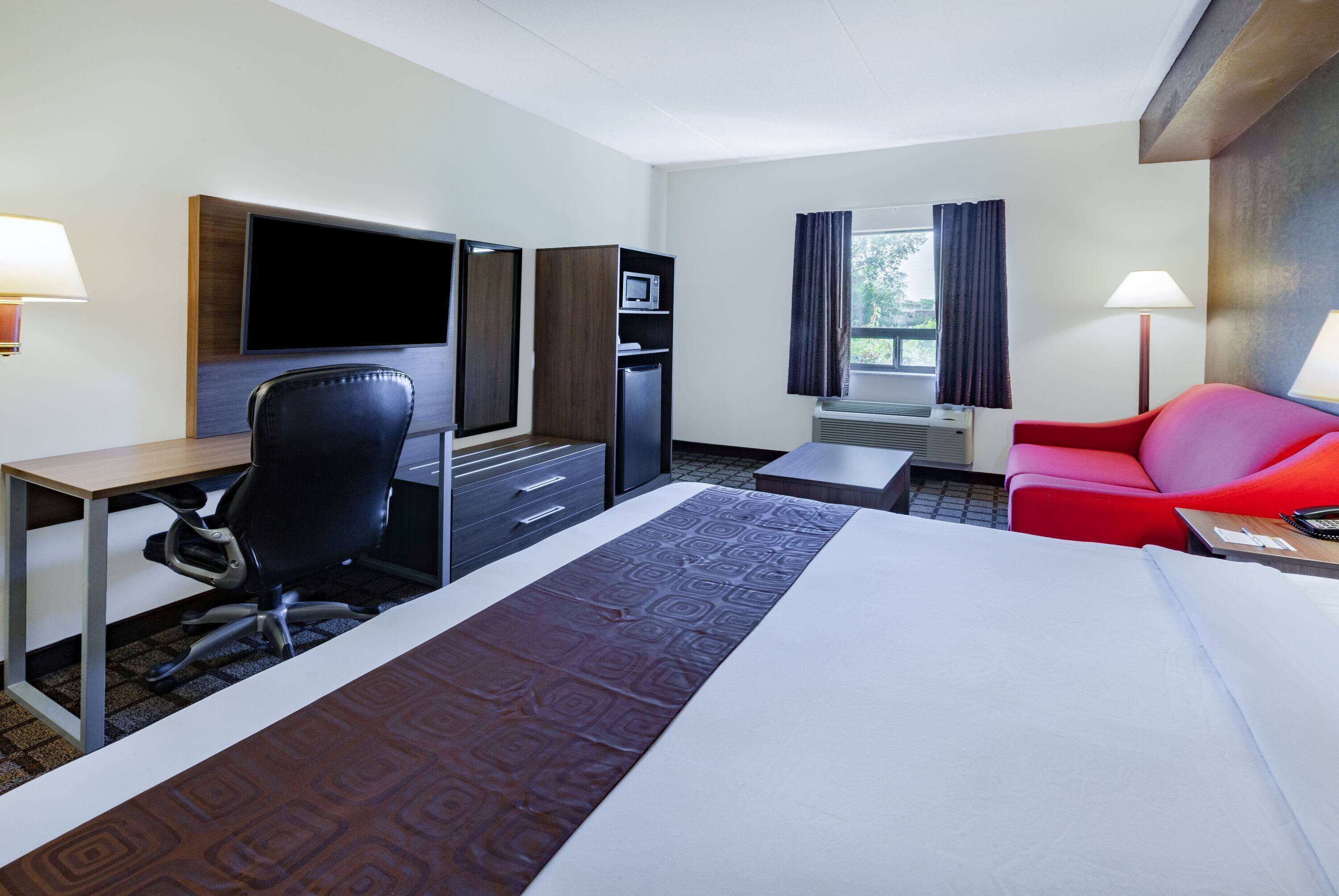 A hotel room with a bed, desk, chair, TV, mini-fridge, and a red couch.