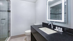 Un baño moderno con cabina de ducha de vidrio, inodoro blanco, encimera negra y un espejo grande con iluminación integrada.