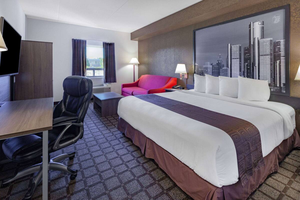 Une chambre d’hôtel avec un grand lit, un bureau, une chaise, un téléviseur et un tableau représentant un paysage urbain accroché au mur.