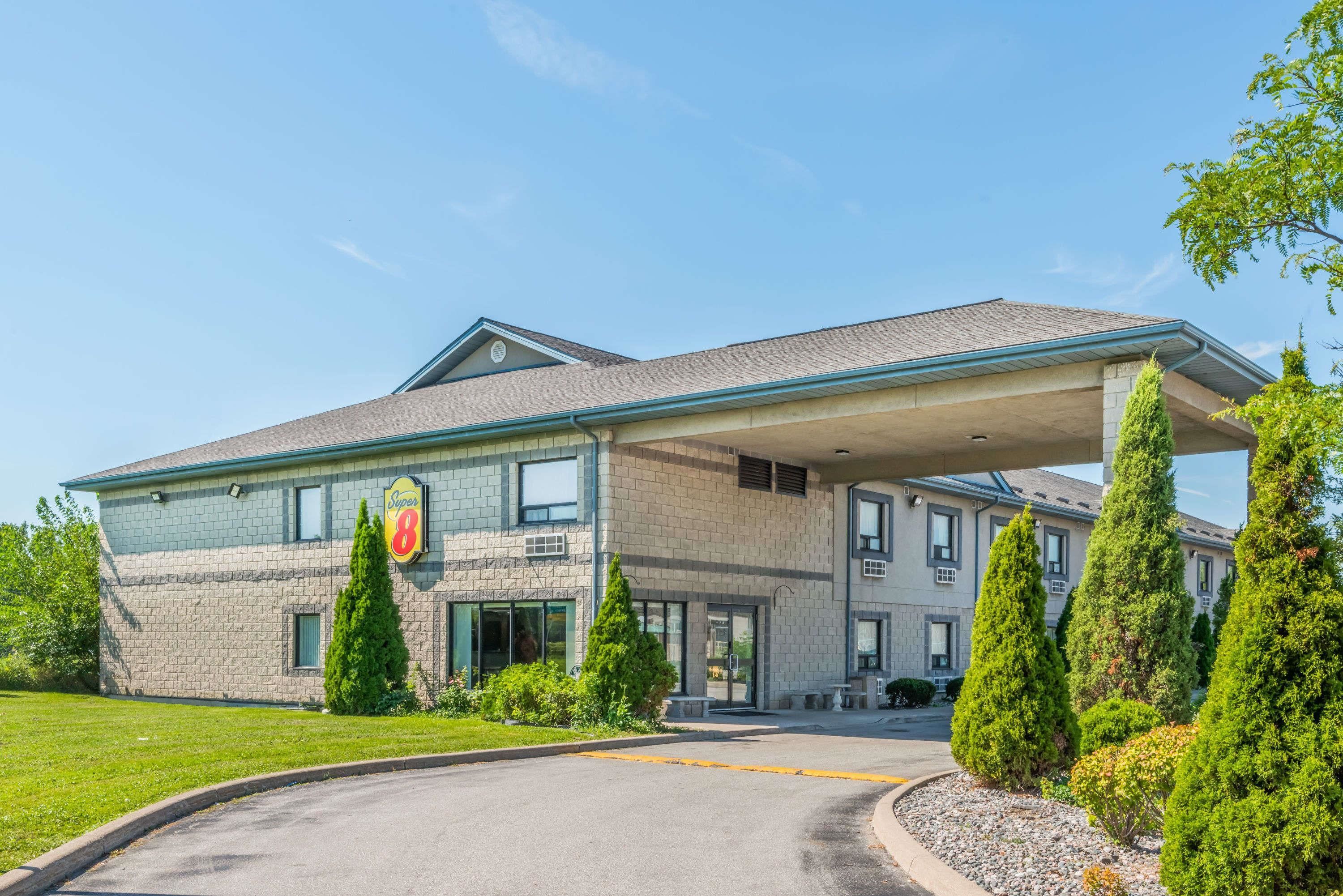 A two-story building with a covered parking area, a sign indicating it is a hotel, and a well-maintained lawn with trees.