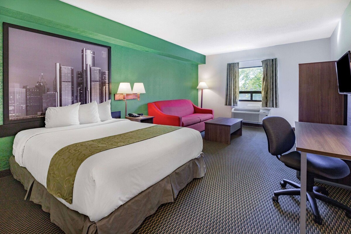 Habitación de hotel con cama, escritorio, silla, sofá rojo, lámpara y televisión.