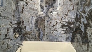 Une salle de bain avec un mur en marbre, une baignoire et des toilettes.