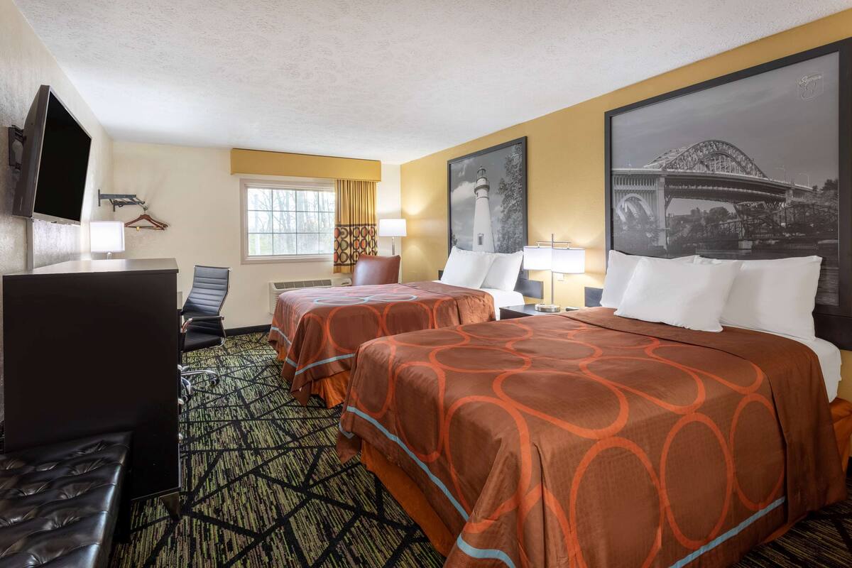 Ein Hotelzimmer mit zwei Betten, einem Schreibtisch, einem Fernseher und einem großen Fenster.