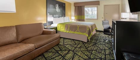 Habitación de hotel con cama, sofá, escritorio con silla, televisión y ventana con cortinas.