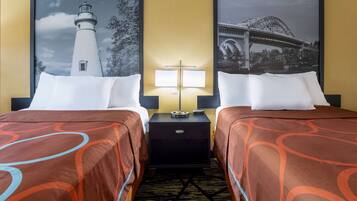A hotel room with two beds, each with a white pillow and a brown patterned bedspread. There is a nightstand between the beds with a lamp and a clock. The walls are yellow, and there are two framed pictures above the beds, one of a lighthouse and the other of a bridge.