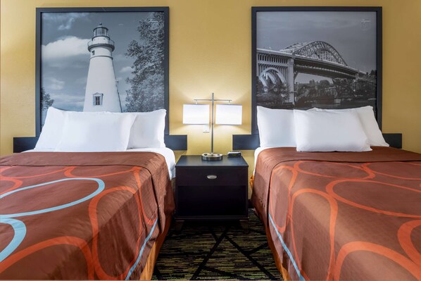A hotel room with two beds, each with a white pillow and a brown patterned bedspread. There is a nightstand between the beds with a lamp and a clock. The walls are yellow, and there are two framed pictures above the beds, one of a lighthouse and the other of a bridge. - Super 8 by Wyndham Wooster (Wooster)