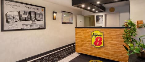 Zona de recepción de un hotel con un mostrador de madera, un cartel de bienvenida enmarcado, un mapa y un suelo de baldosas.