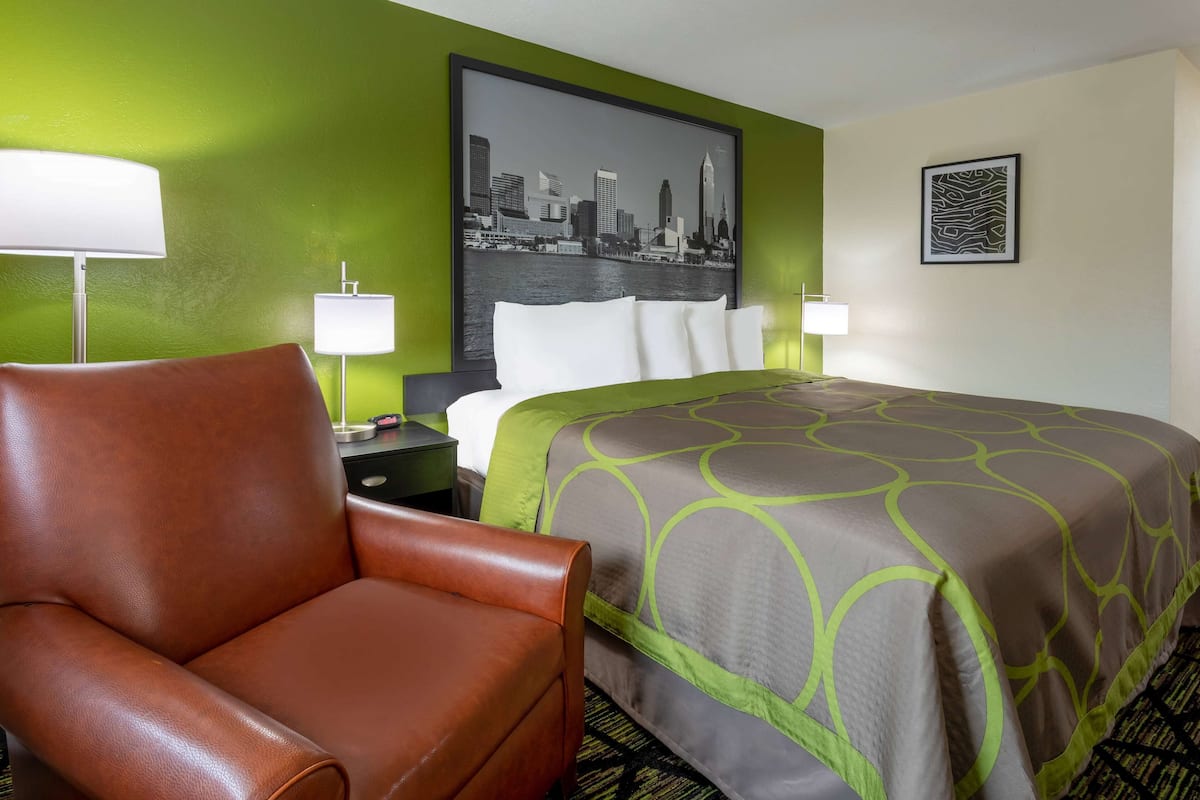 Ein Hotelzimmer mit einem Bett, einem braunen Ledersessel, zwei Nachttischlampen, einer grünen Wand und einem Stadtbild an der Wand.