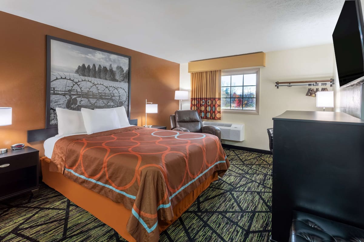 Ein Hotelzimmer mit einem großen Bett, einem Schreibtisch, einem Stuhl, einem Fernseher und einem Fenster mit Vorhängen.