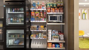 A vending machine with various snacks and drinks, a microwave, and shelves stocked with food items. - Spark By Hilton Woodstock (Woodstock)
