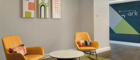 A modern lobby with two orange rocking chairs, a round table, and abstract wall art.