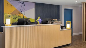 A hotel reception desk with a modern design, featuring a large abstract artwork on the wall, a wooden reception desk, and two illuminated lamps. - Spark By Hilton Woodstock (Woodstock)