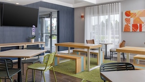 A modern hotel lobby with multiple seating areas, a flat-screen TV, and a large window with curtains. - Spark By Hilton Woodstock (Woodstock)