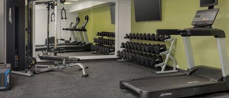 A gym with cardio equipment, dumbbells, and a treadmill.