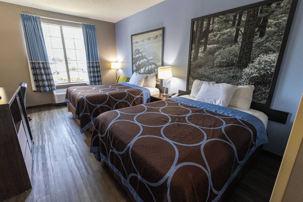 Habitación de hotel con dos camas, un ventanal con cortinas, un cuadro en la pared y un escritorio con silla.