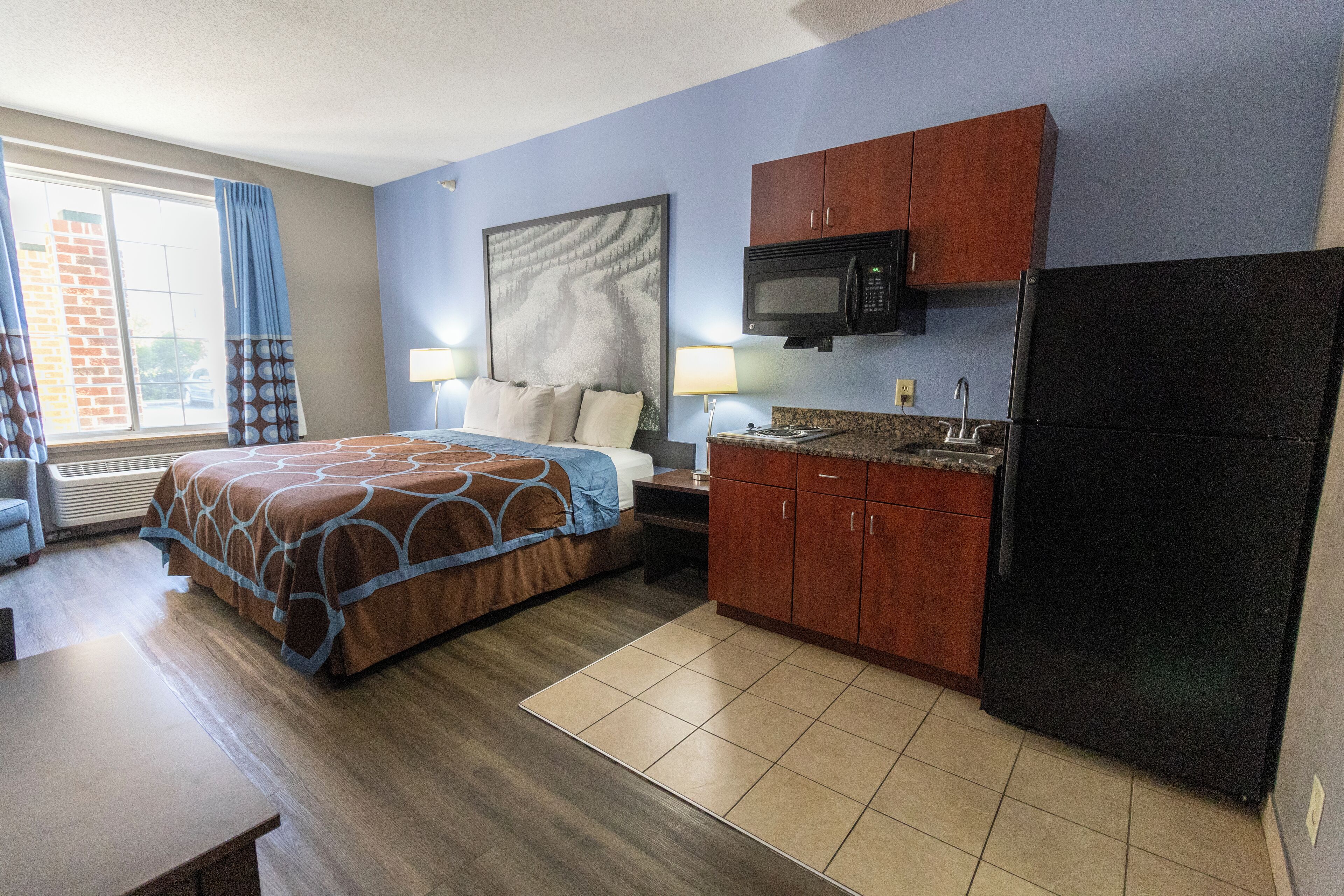 A hotel room with a bed, a desk, a microwave, a refrigerator, and a window with curtains.