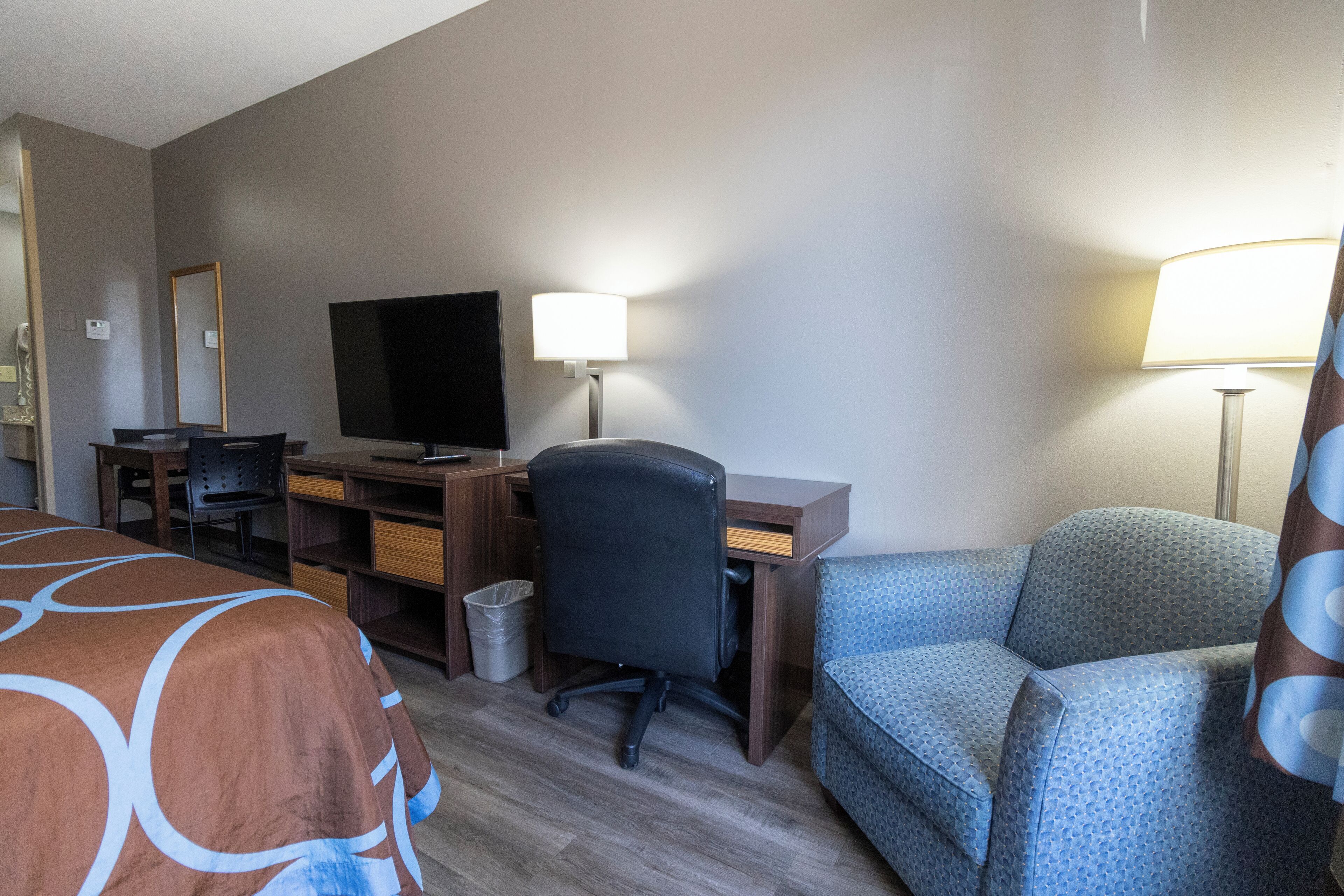A hotel room with a bed, a desk with a computer, a television, two chairs, and a lamp.