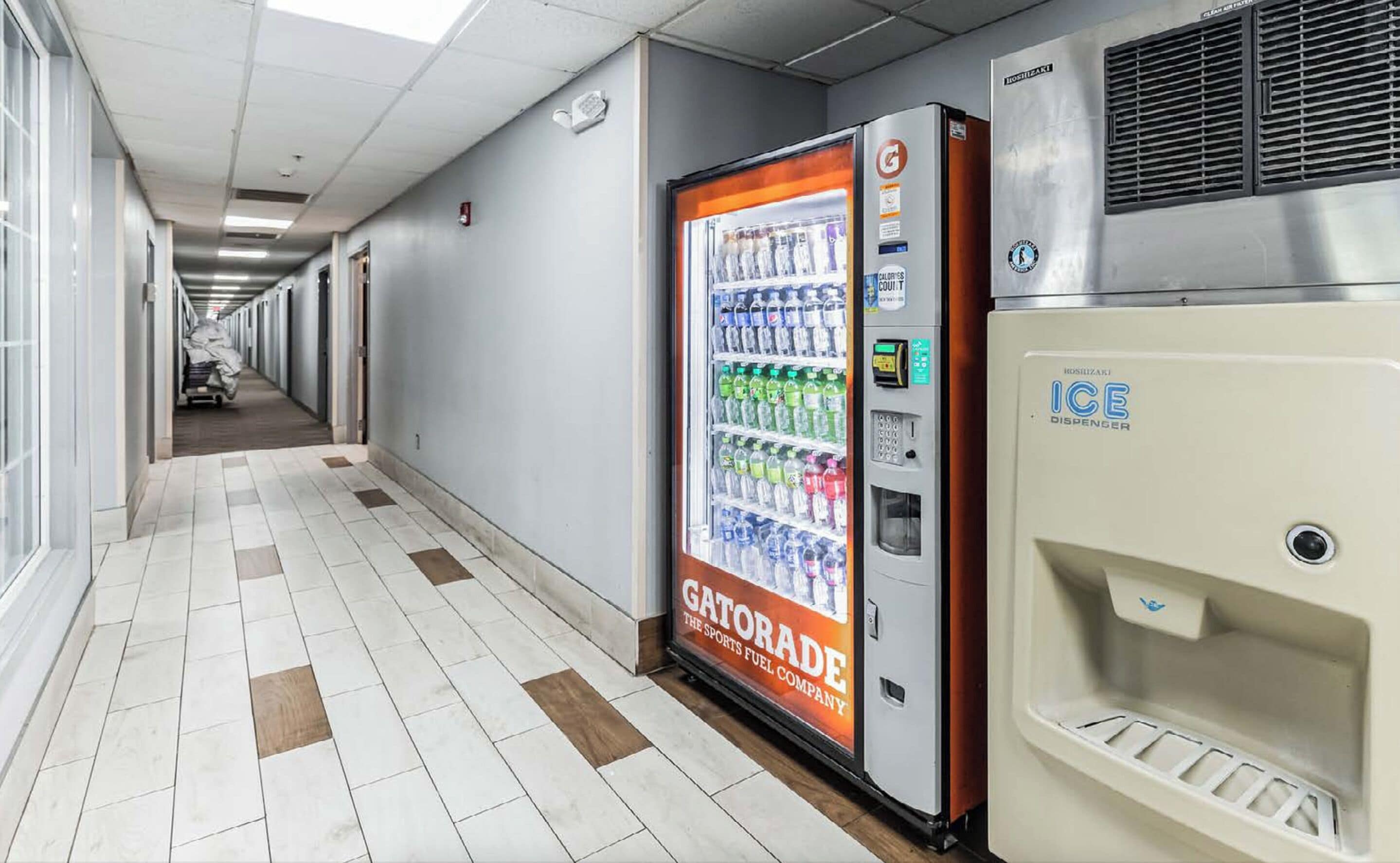 A hallway with a vending machine stocked with beverages and an ice dispenser.