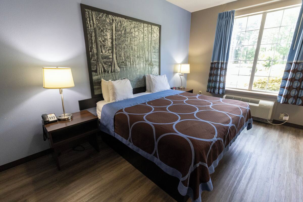 Habitación de hotel con una cama grande, dos lámparas de noche, un teléfono en la mesita y un amplio ventanal con cortinas.