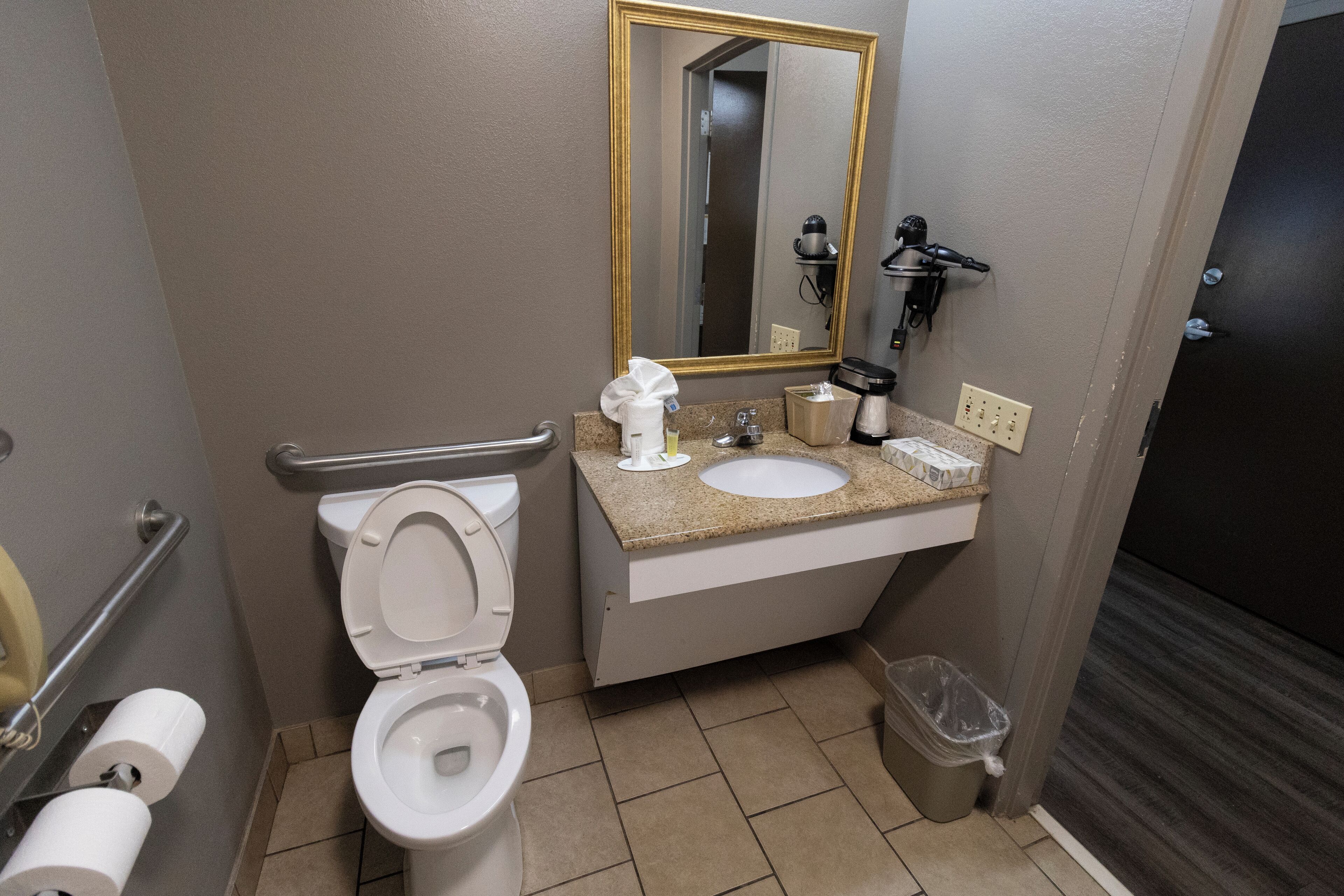 A bathroom with a toilet, sink, mirror, and hand dryer.